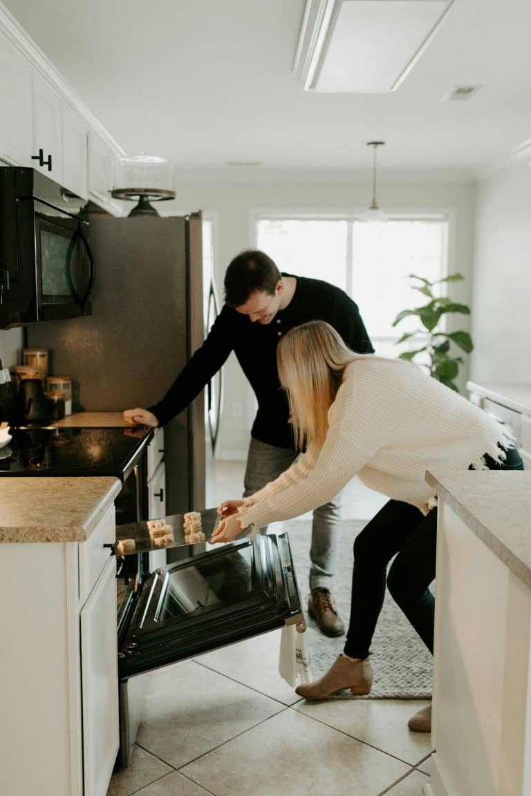 Women putting cookies to bake in oven.